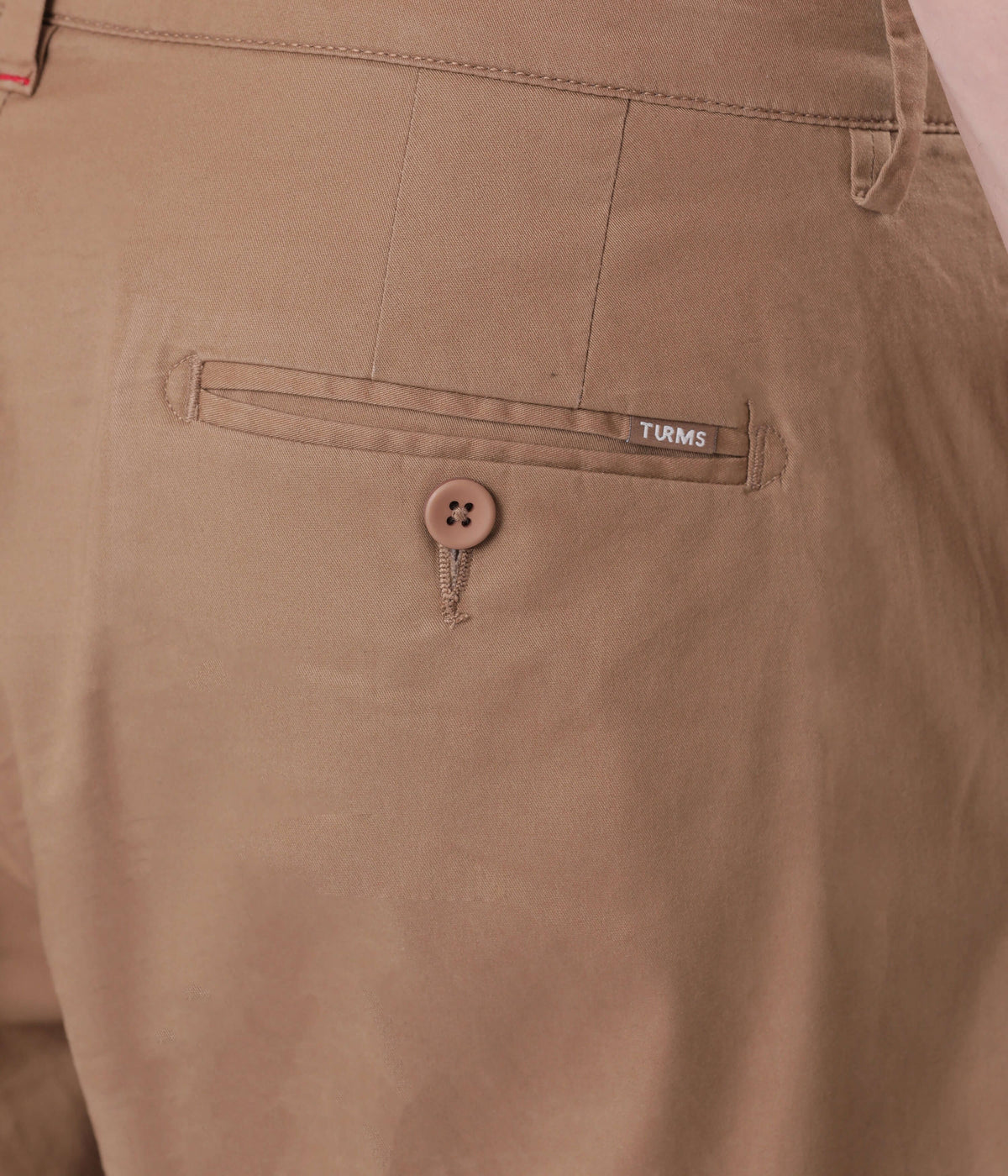 Close-up of a Turms Chino's back pocket showcasing button detail and brand label, highlighting style and quality.