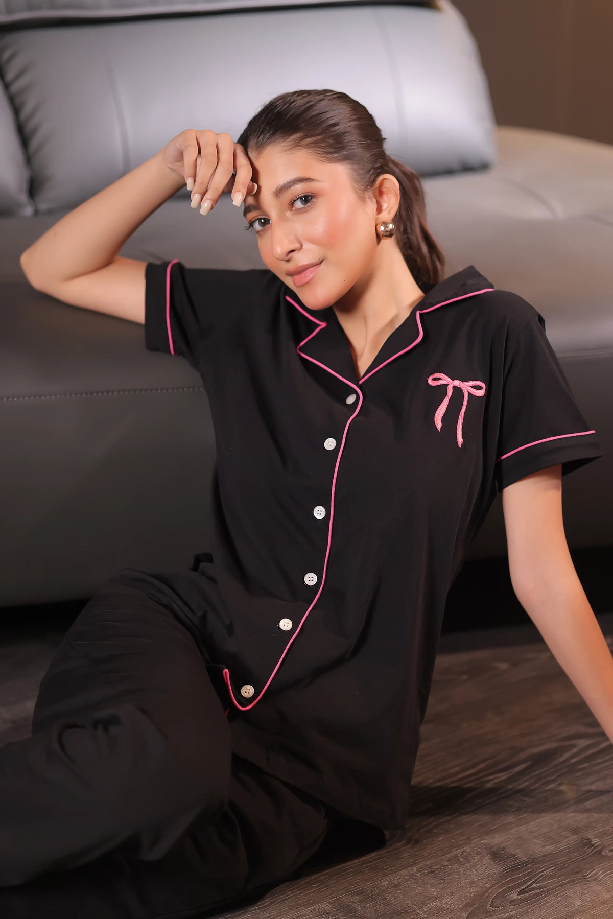 Woman wearing a black pajama set with pink accents sitting on a couch.
