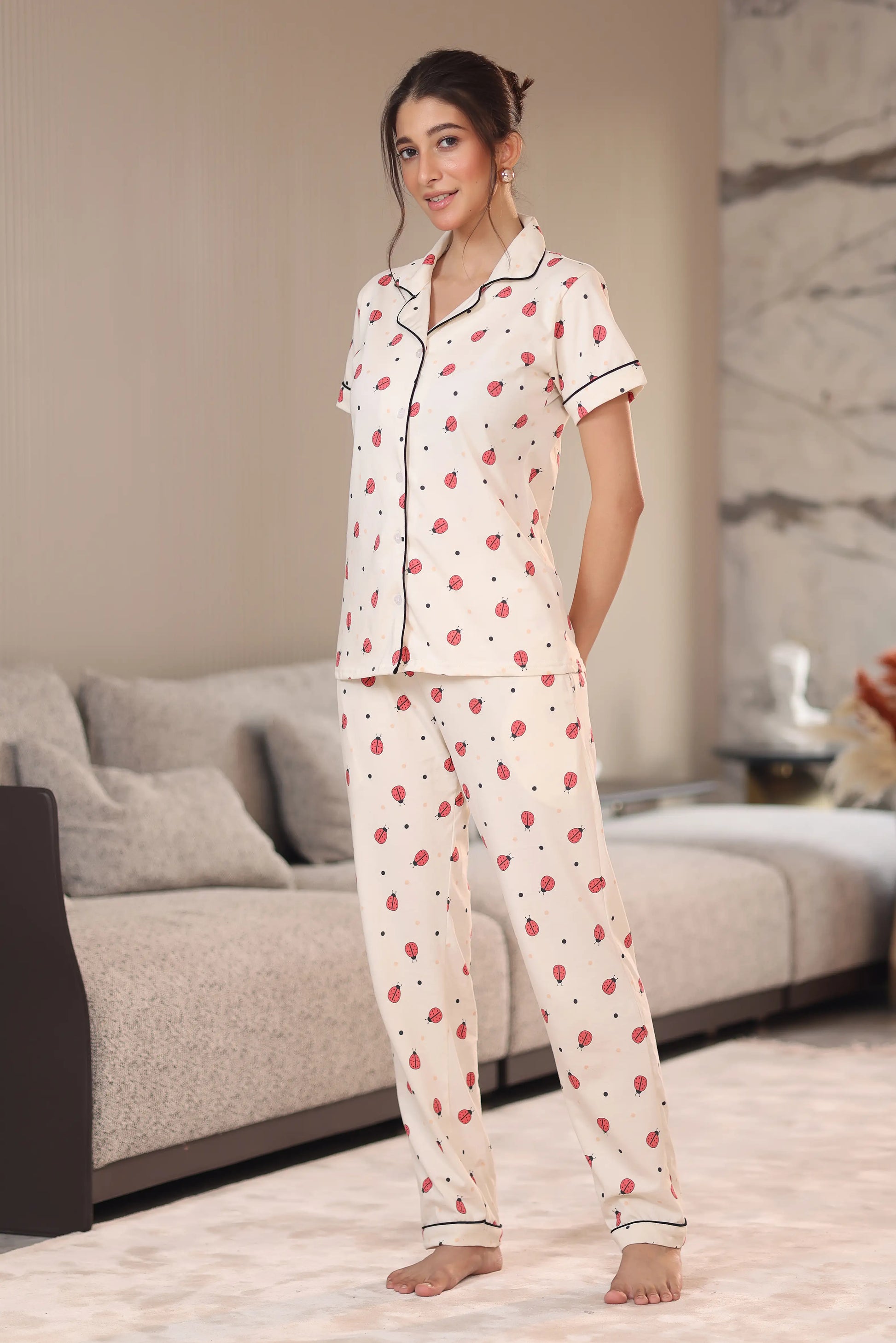 Woman wearing a white pajama set with red patterns in a living room.
