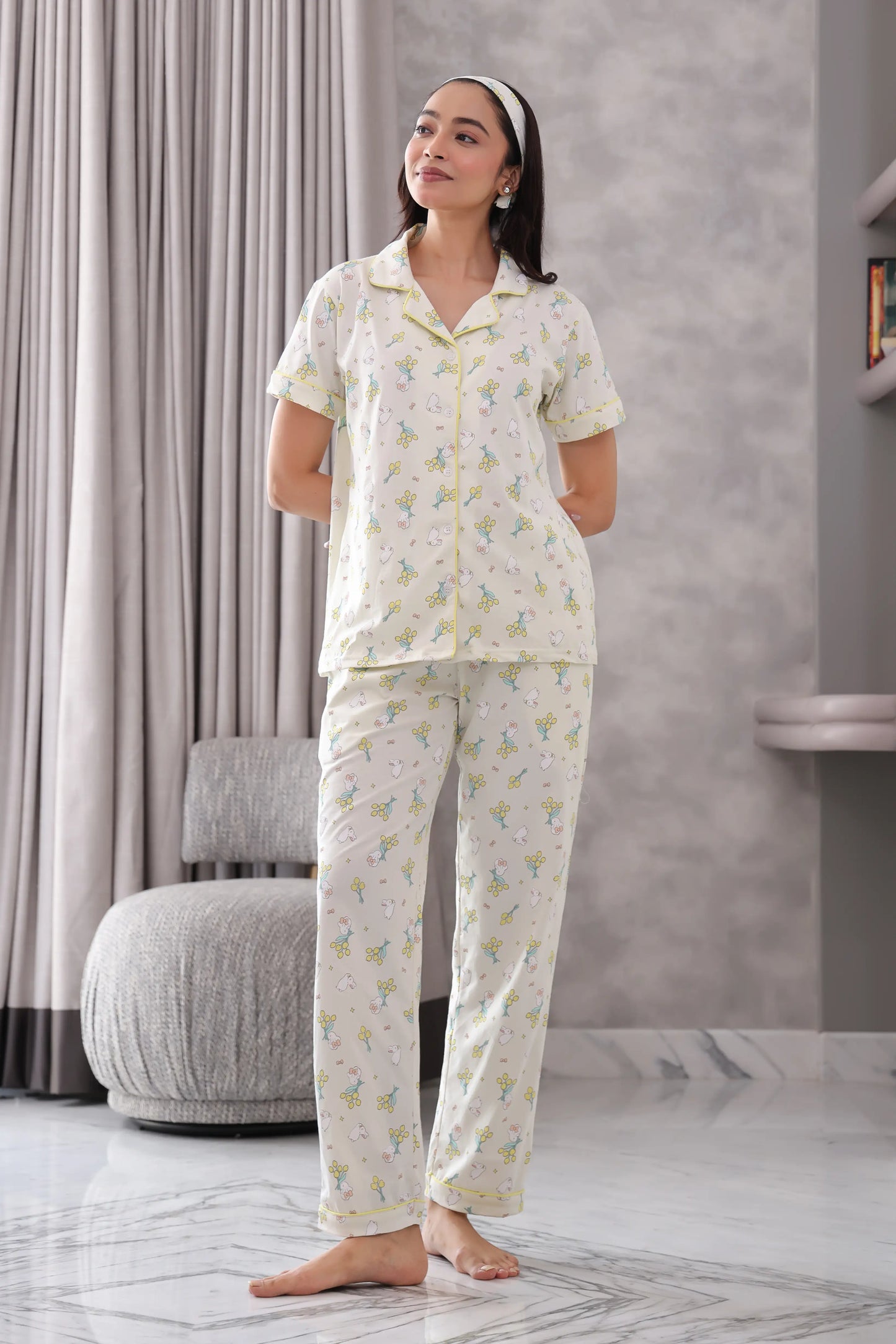 Woman wearing a white pajama set with a subtle pattern in a room with gray curtains and a marble floor.