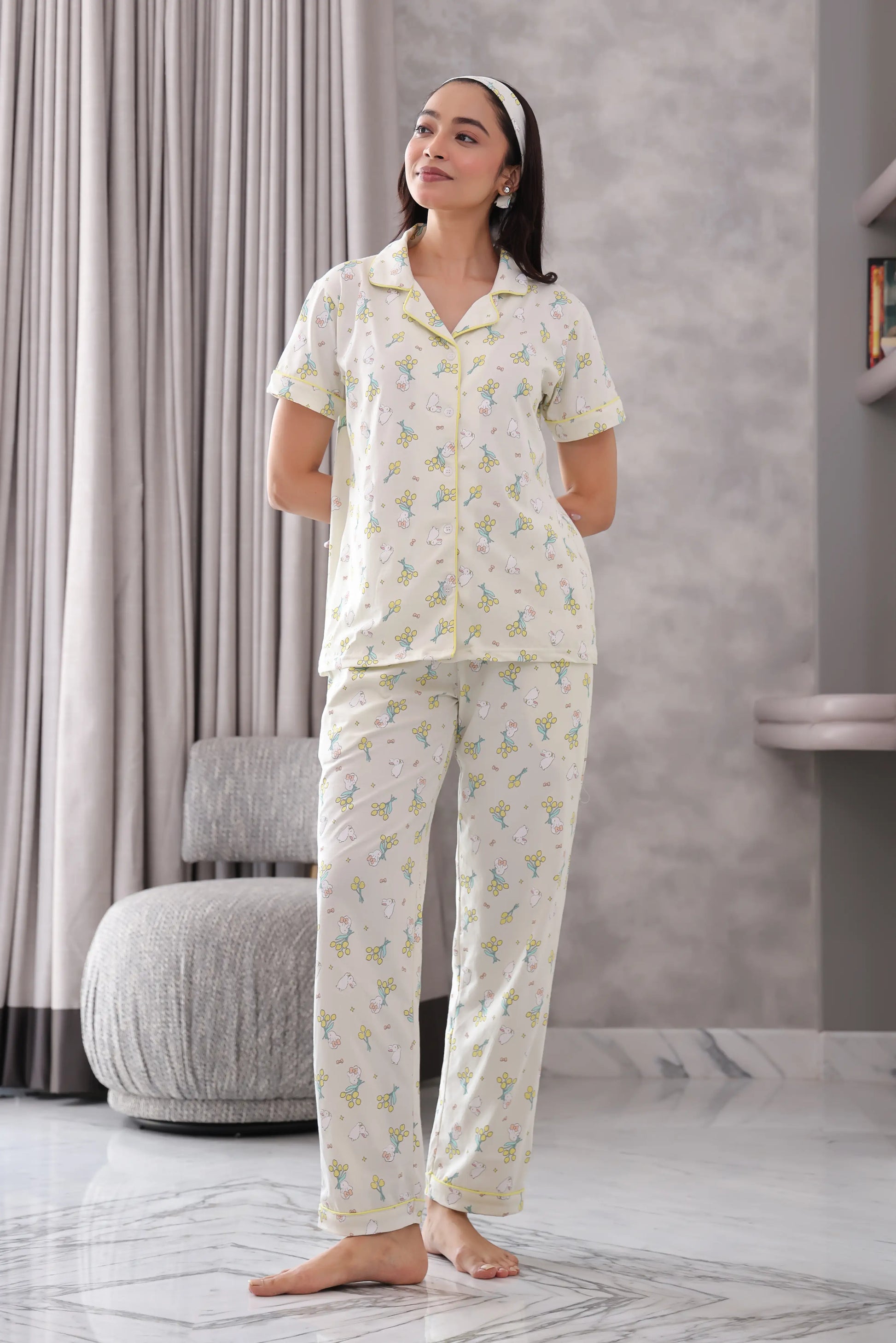 Woman wearing a white pajama set with a subtle pattern in a room with gray curtains and a marble floor.