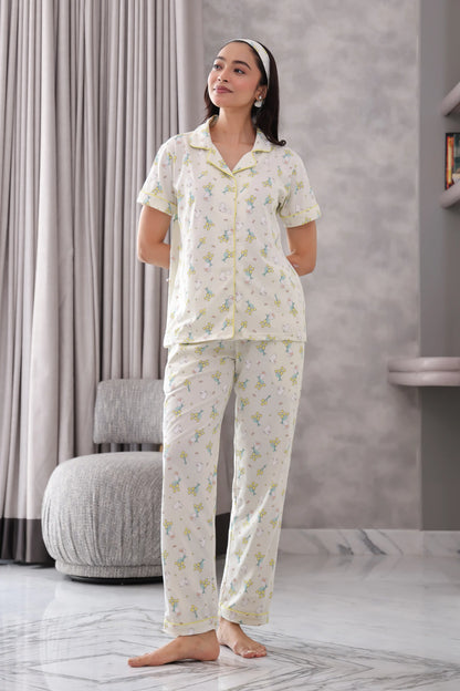 Woman wearing a white pajama set with a subtle pattern in a room with gray curtains and a marble floor.