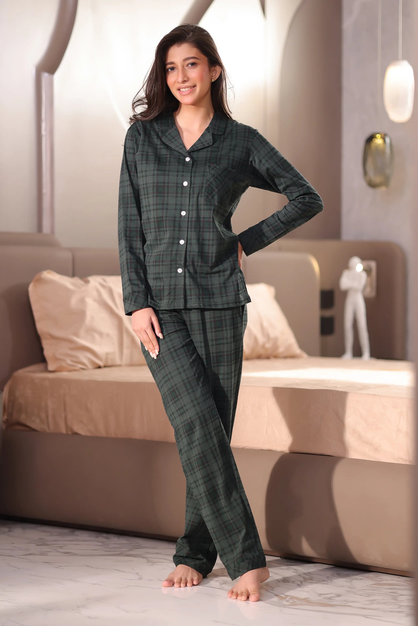 A woman wearing a green plaid pajama set in a bedroom.