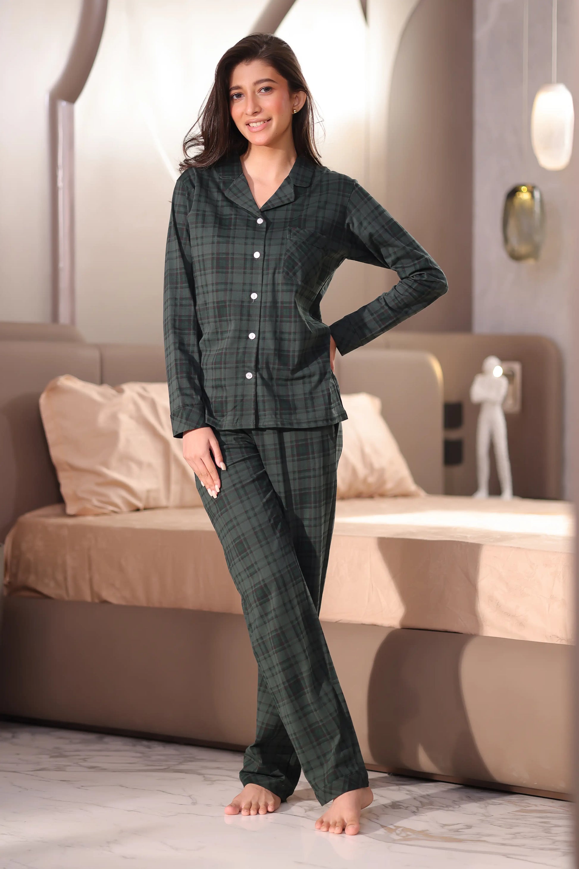 A woman wearing a green plaid pajama set in a bedroom.