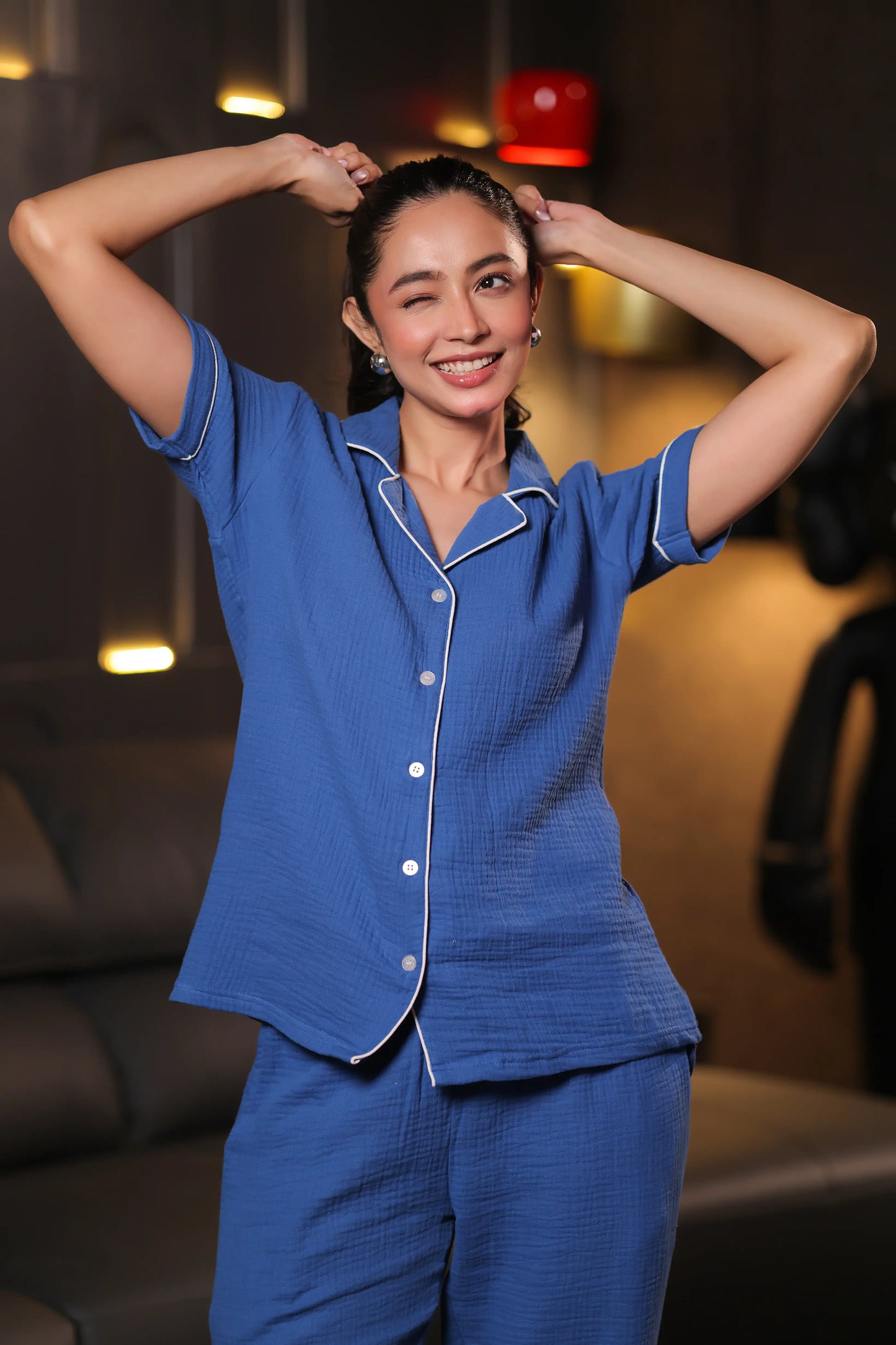 Woman wearing a blue pajama set in a dimly lit room.