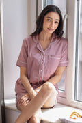 Woman wearing pink shorts set sitting by a window