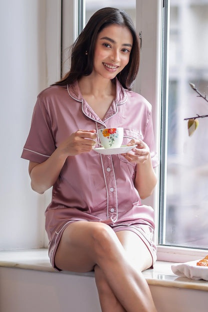 Woman in pink shorts set holding a floral teacup by a window